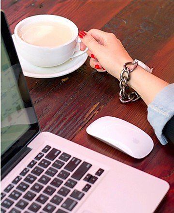 Hand holding a cup of coffee next to a laptop