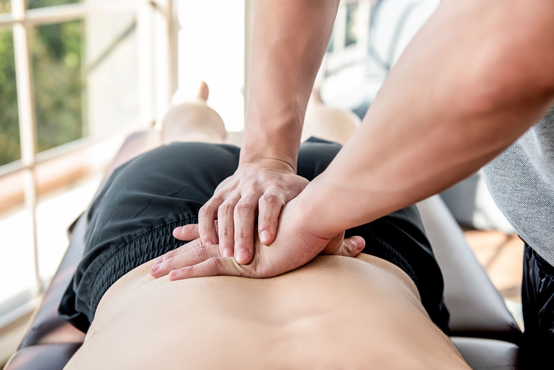 Hands applying pressure to a person's lower back during a massage on a massage table.