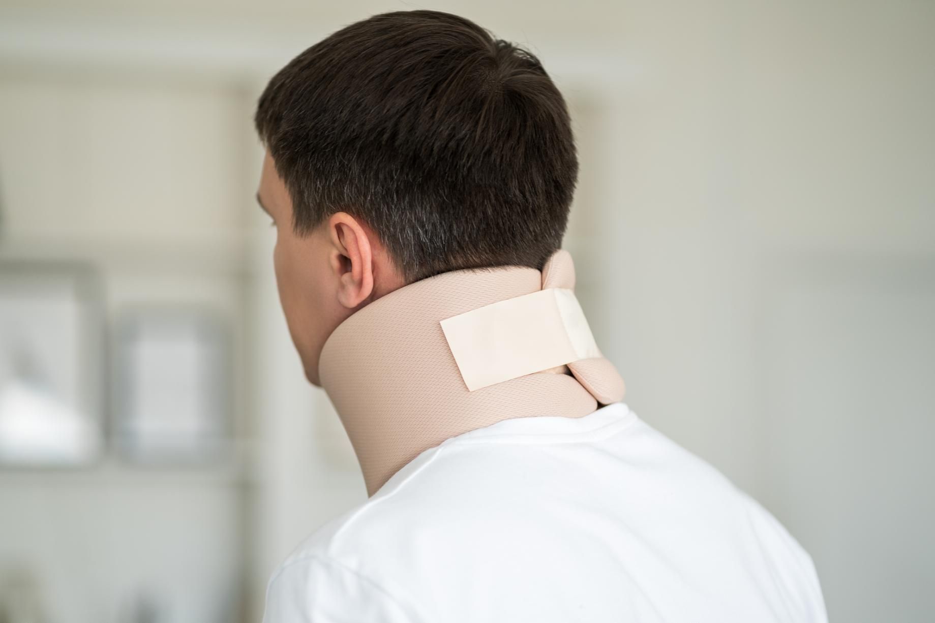 Man wearing a neck brace, viewed from the back. Beige brace with a tan strap.