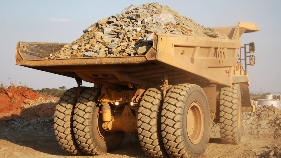 A large yellow dump truck is sitting in the dirt