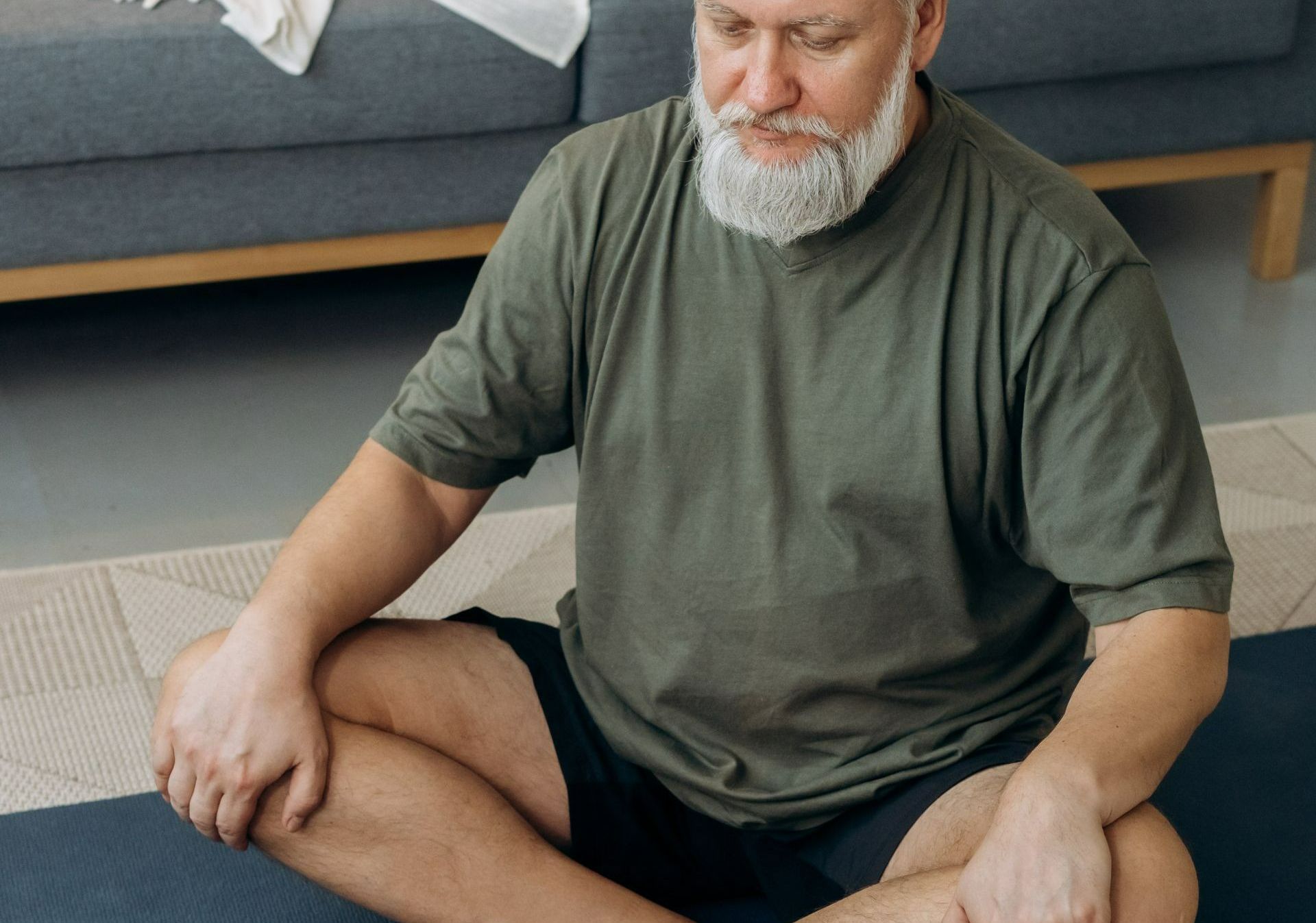 Een man met een baard zit met zijn benen over elkaar op een yogamat.