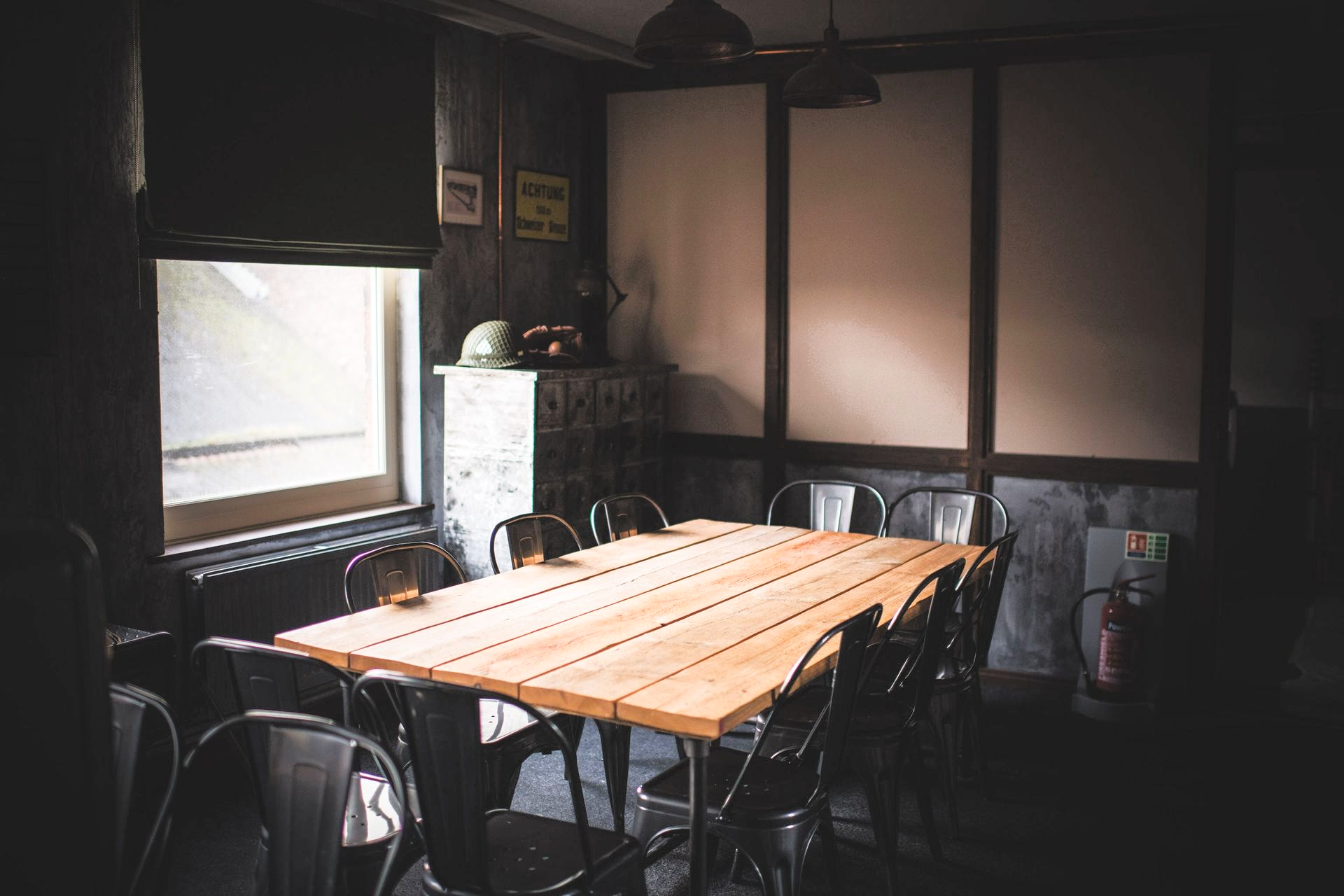 A dimly lit dining room with a long wooden table and metal chairs.