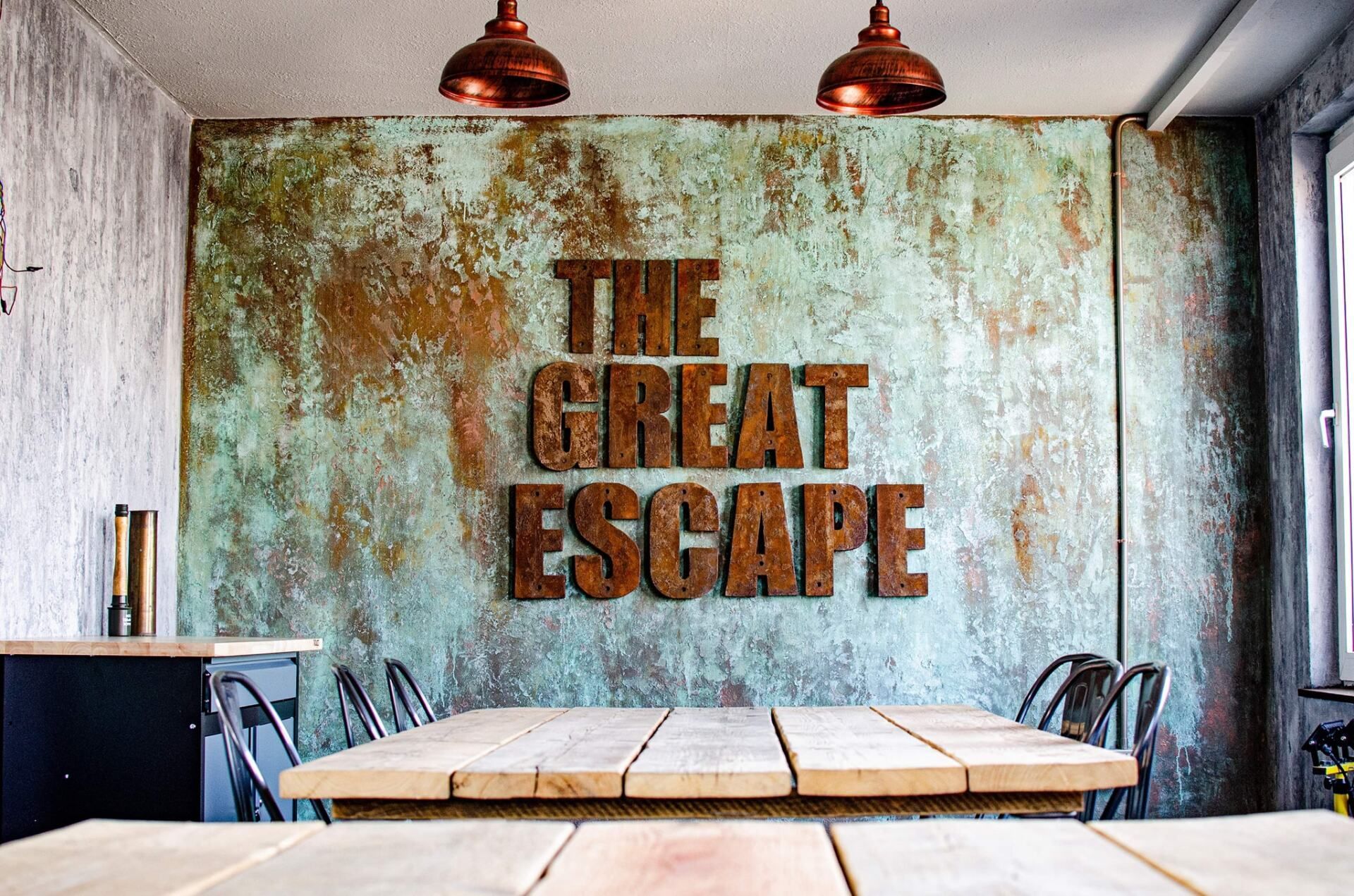 Rustic room with a wooden table, chairs, and "The Great Escape" sign on a distressed wall.
