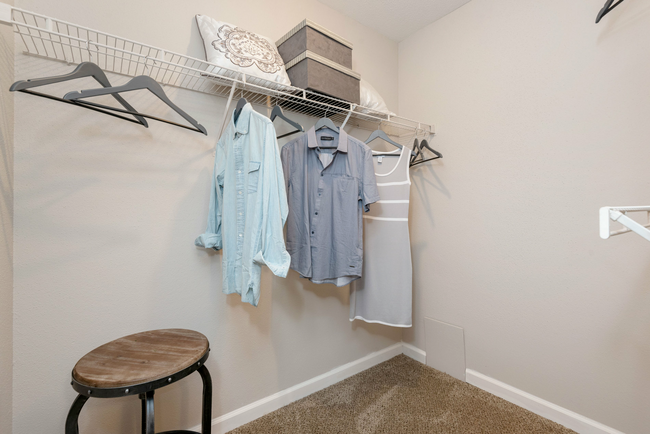 A walk in closet with clothes hanging on the wall and a stool.