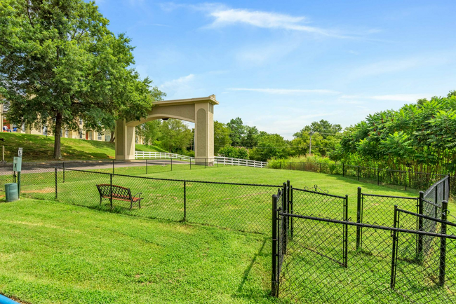 A dog park with a chain link fence and a bridge in the background.