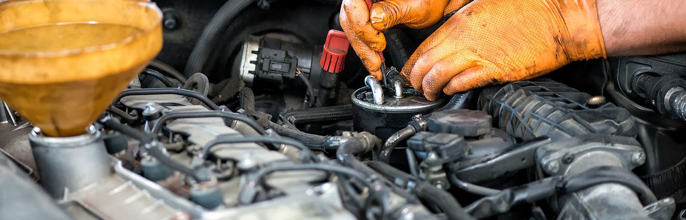 Mechanic using a wrench on a car engine with orange gloves in a garage