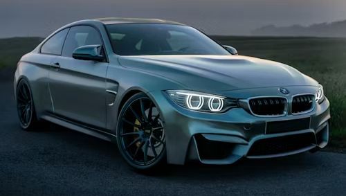 Silver BMW M4 coupe on a road, headlights illuminated.