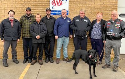 Hage-Kobany employees are posing for a picture with a black dog .