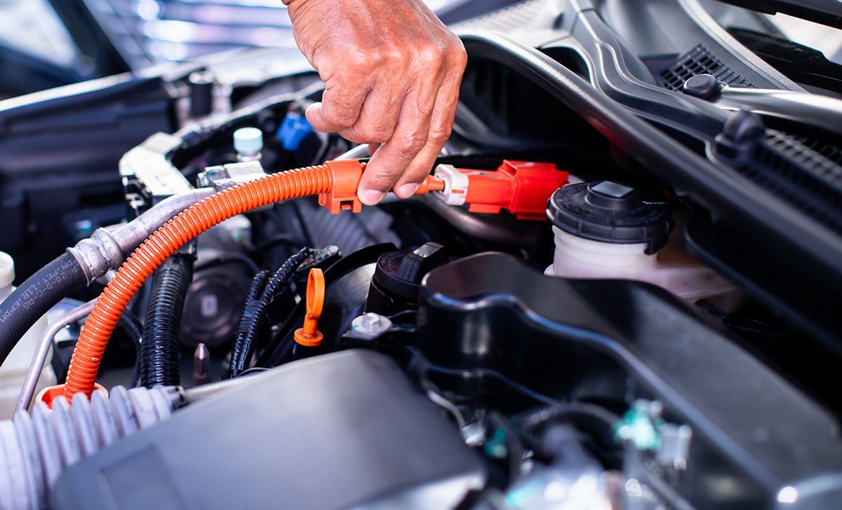 Hand connecting orange cable to a red car battery terminal in an engine bay.