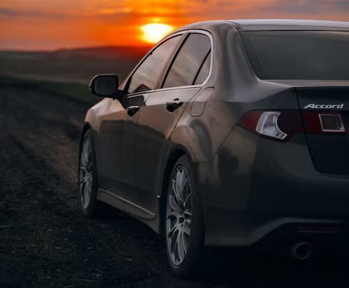 Dark gray sedan parked on a road at sunset, with orange sky in the background