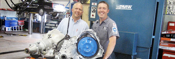 Two men are holding a large engine in a garage.