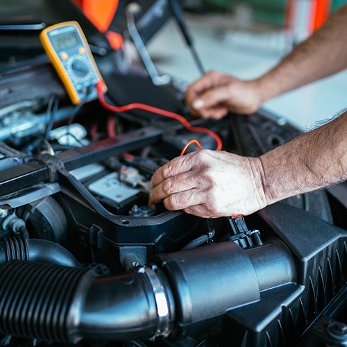 A man is working on a car engine with a multimeter.