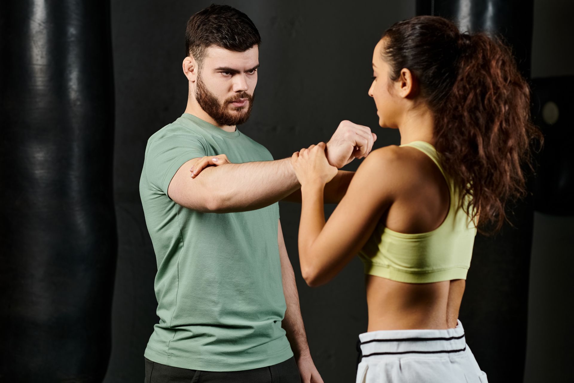 A male trainer teaches self-defense techniques to a woman in a gym setting. A male trainer teaches self-defense techniques to a woman in a gym setting.
