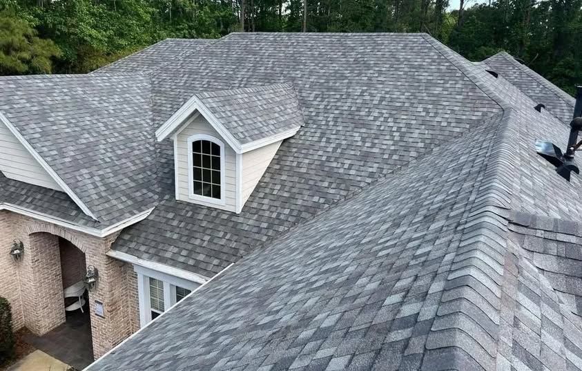 Gray shingle roof on a house with a white dormer and brick siding, seen from above.