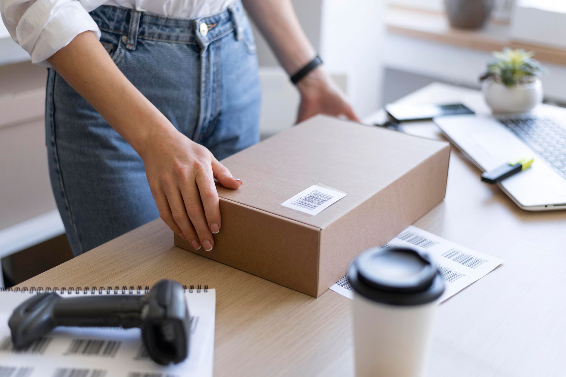 A woman is holding a cardboard box on a desk.