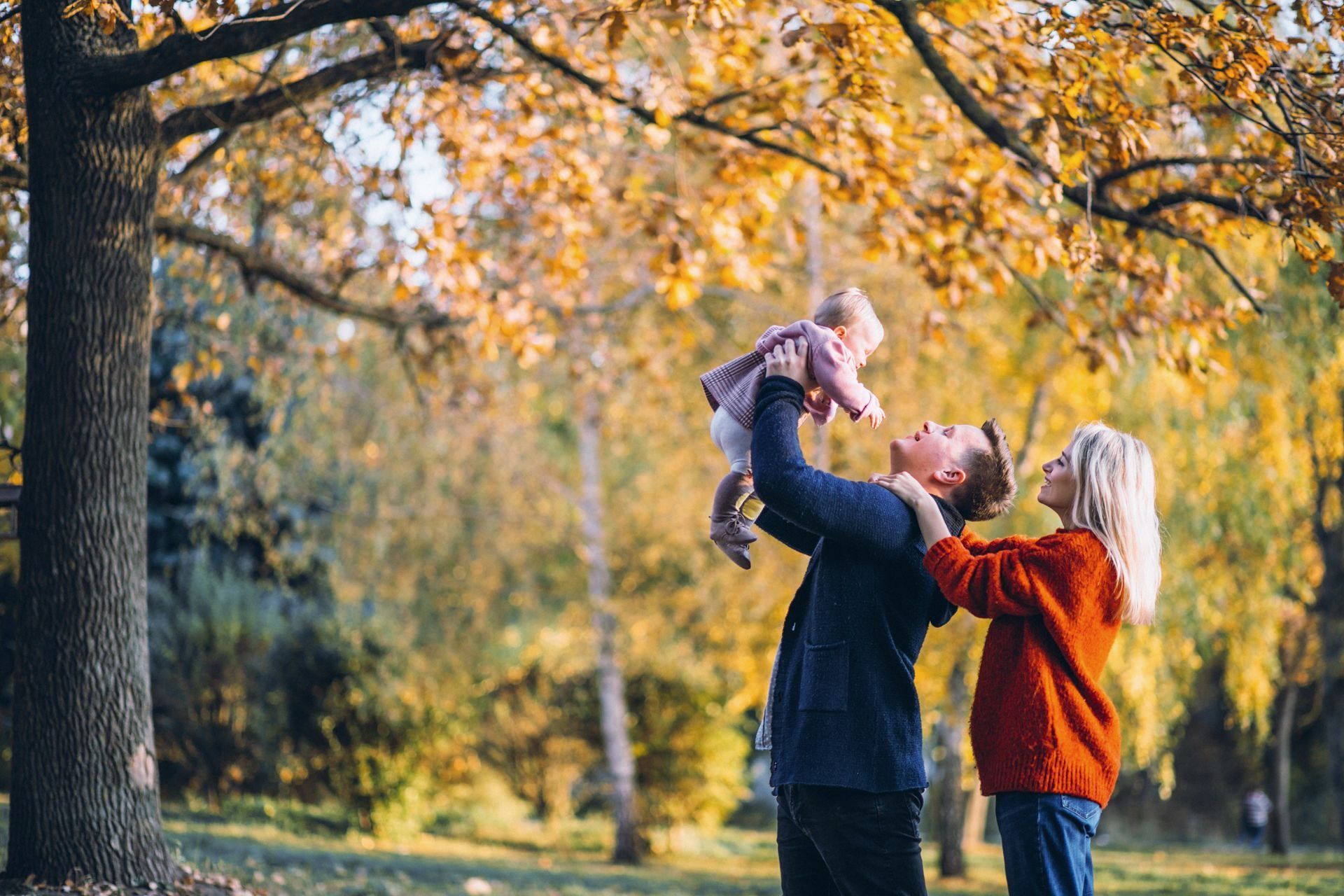 A man and woman are holding a baby in their arms in a park.