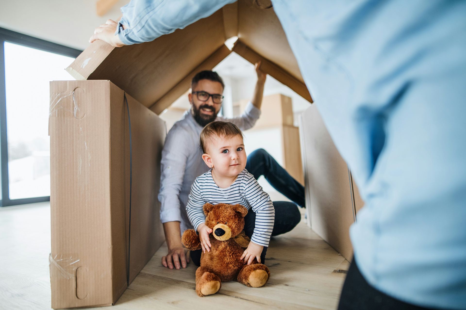 A man and a child are playing in a cardboard house.