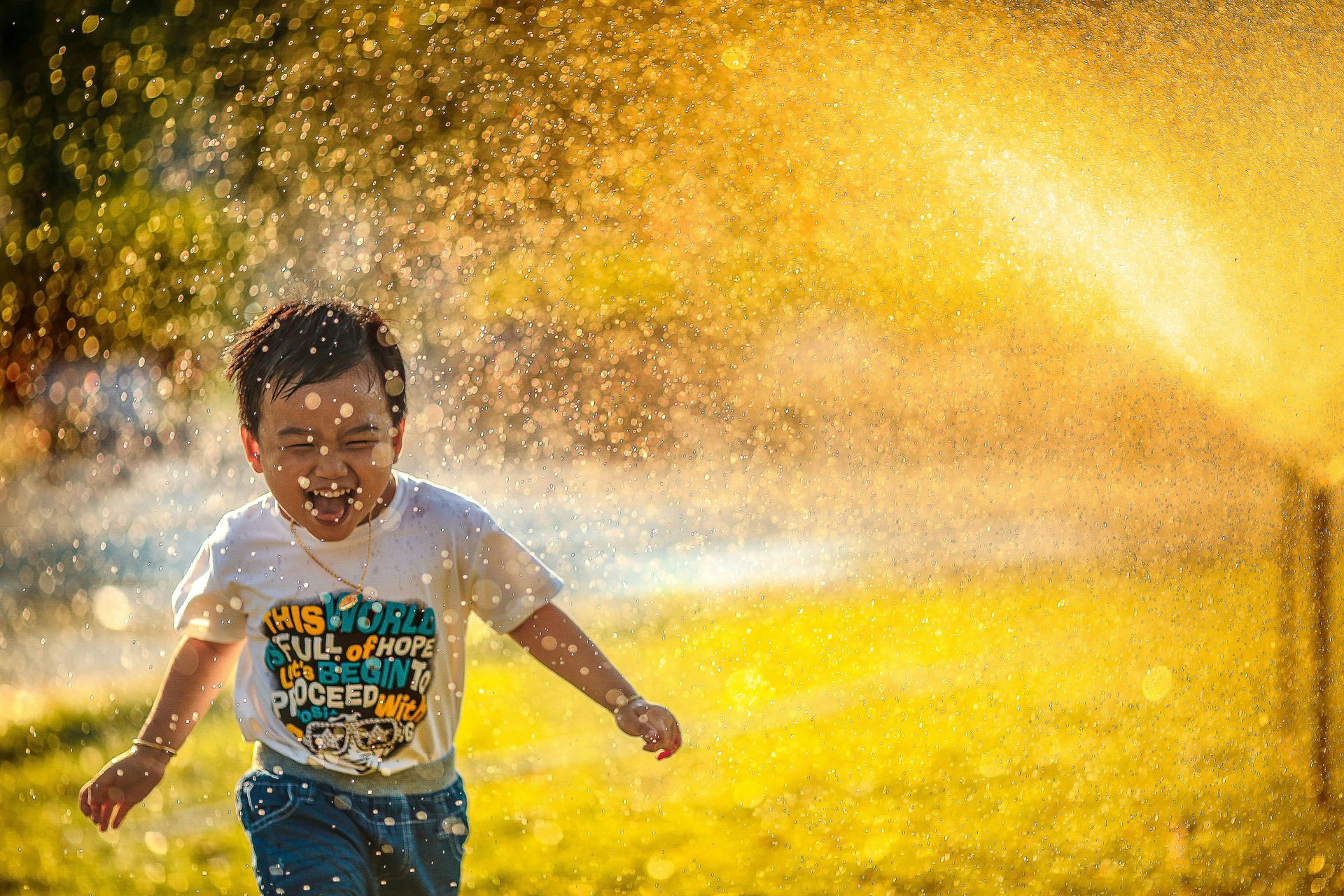 A young boy is running through a sprinkler in a park.