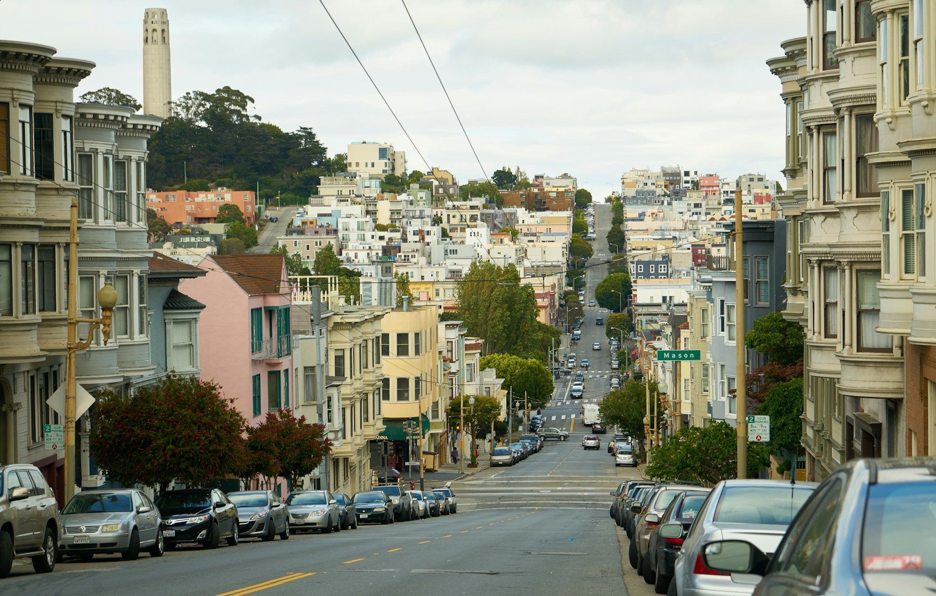 A row of cars are parked on the side of a city street