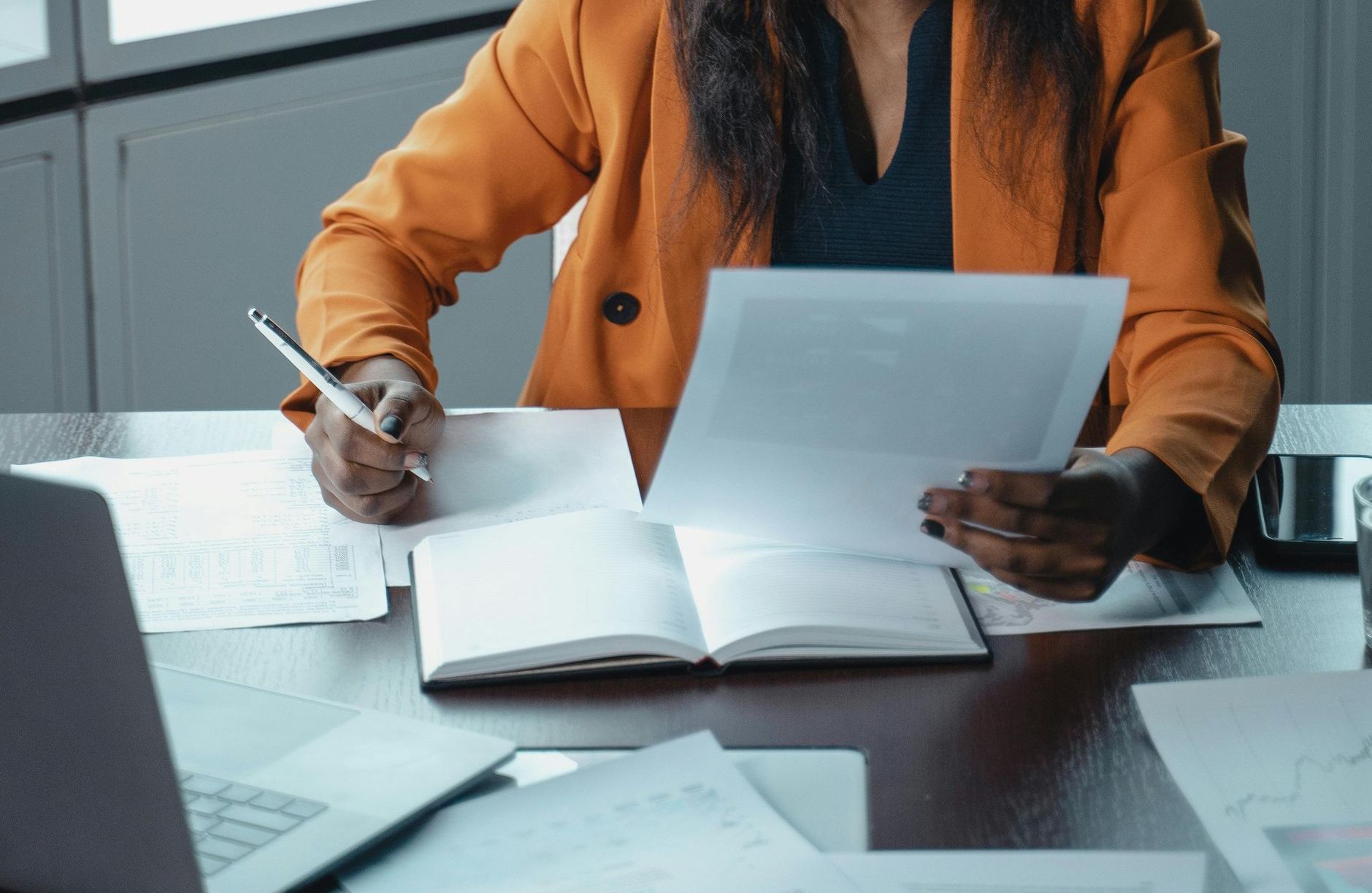 A woman is sitting at a desk holding a pen and a piece of paper.