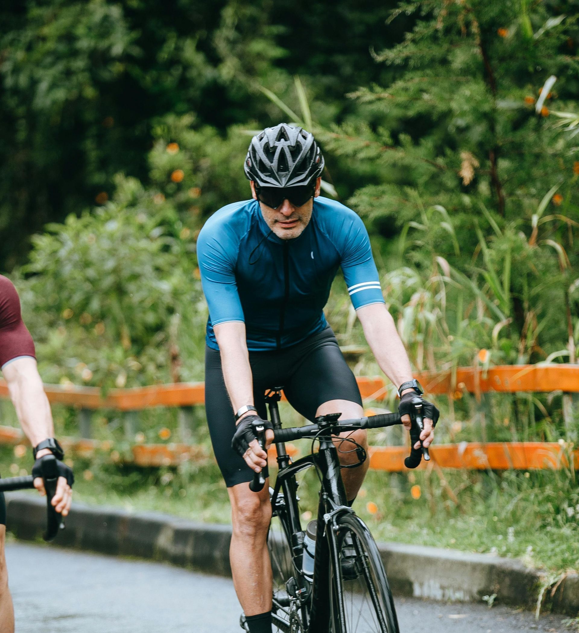 A man is riding a bike down a road next to another man.