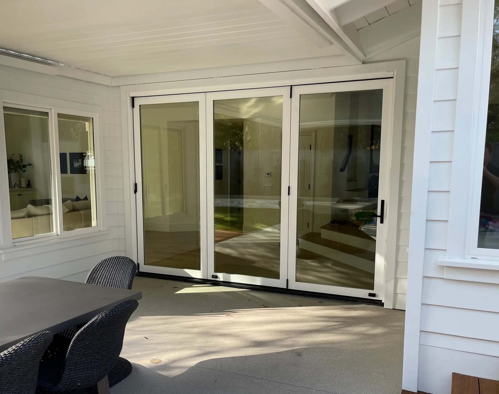 A white house with a patio with a table and chairs and sliding glass doors.