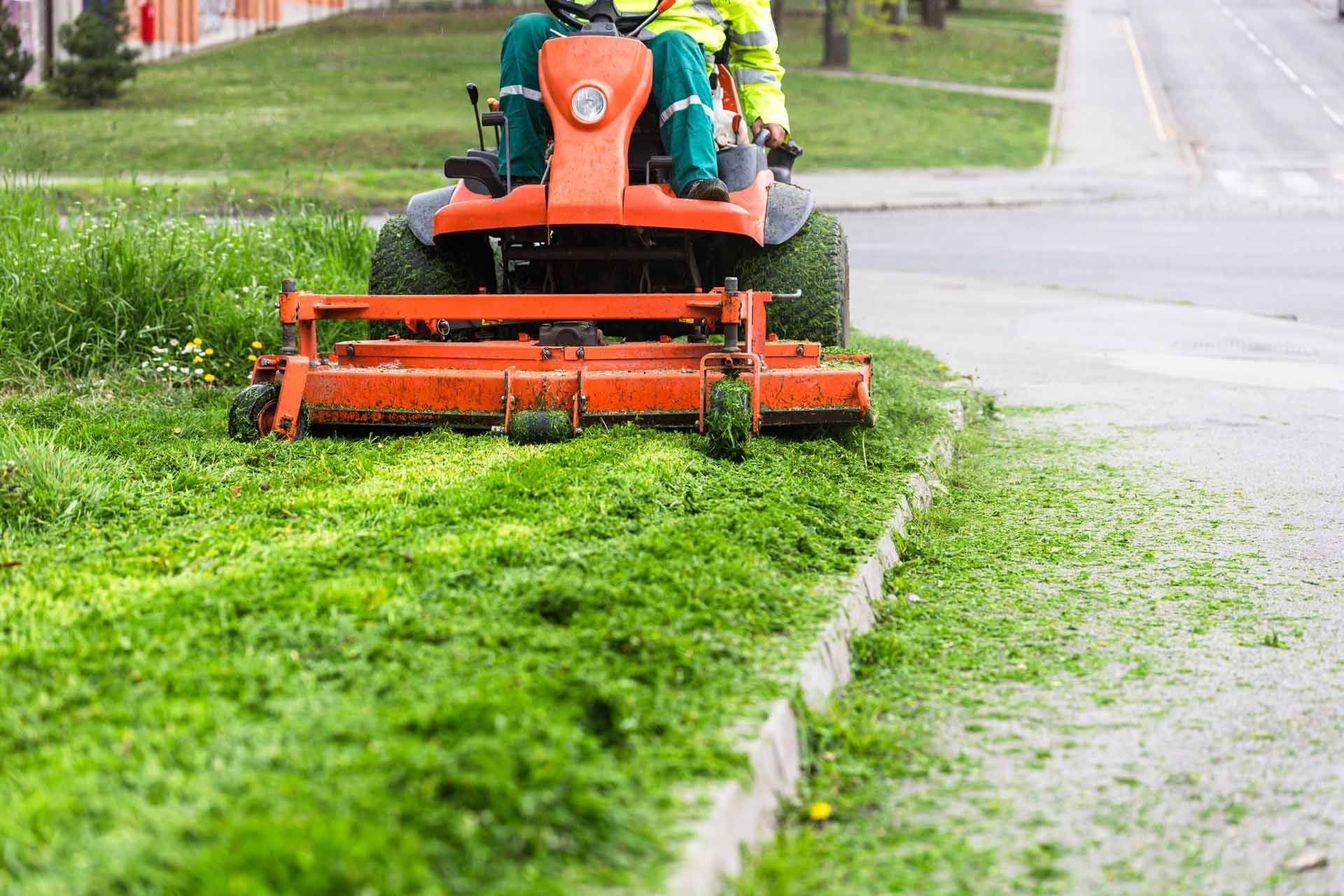 A man is riding a lawn mower on a sidewalk