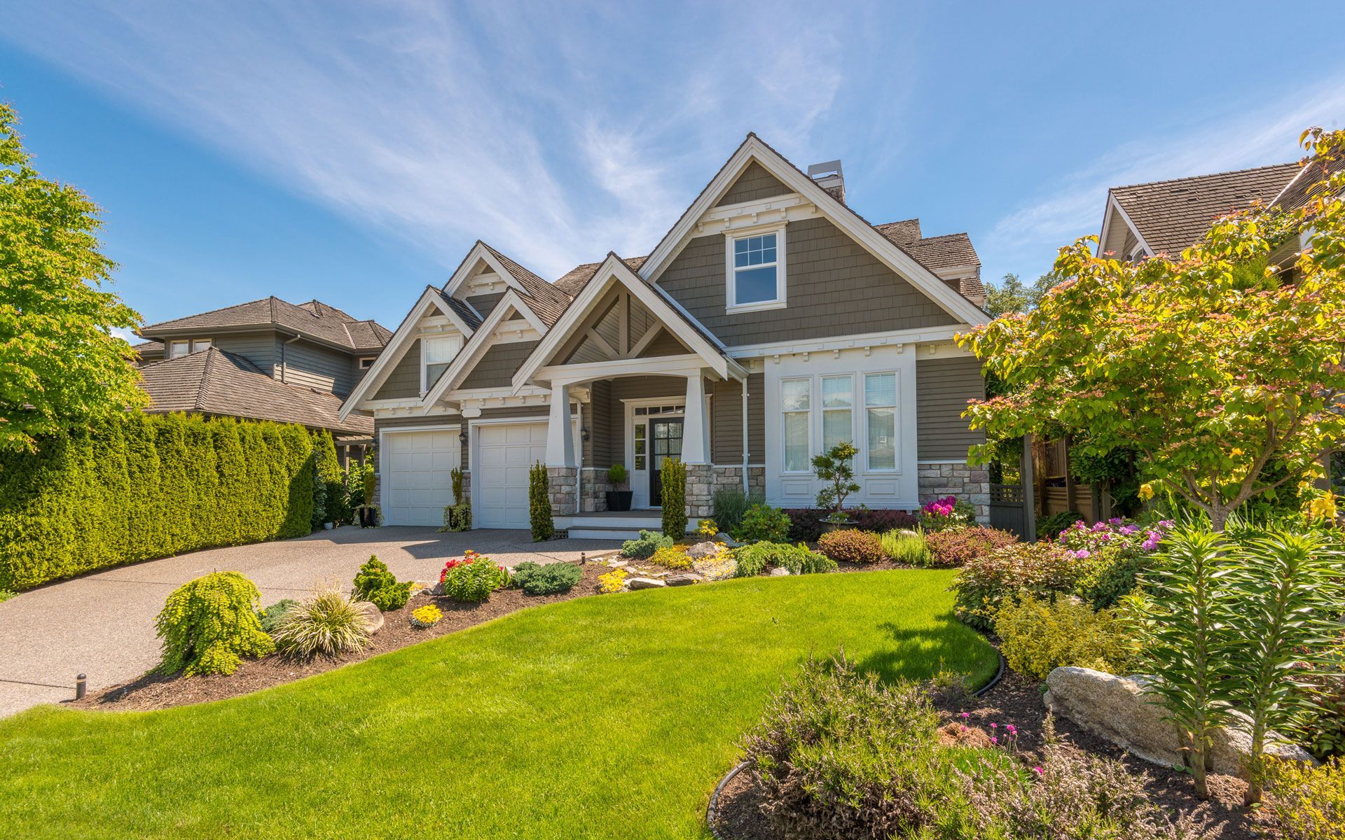 Green house with a well-manicured lawn and garden under a bright blue sky.