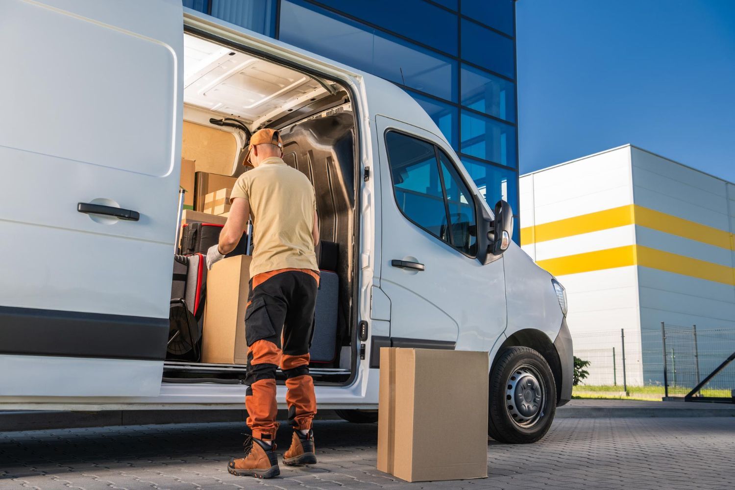 Delivery person loading boxes into a white van near a modern building.