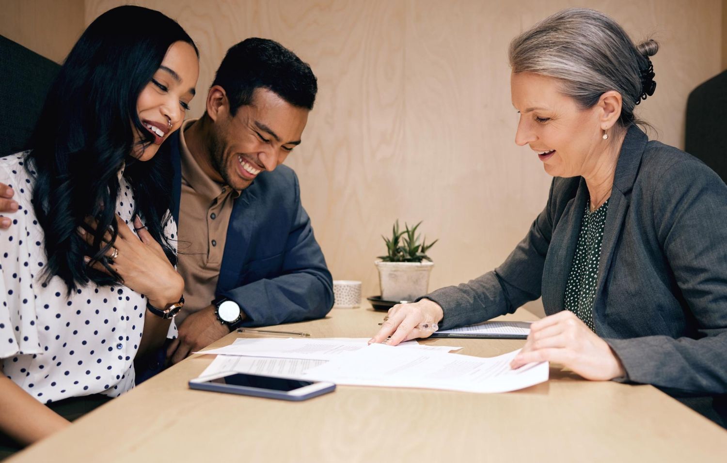 Couple smiles while reviewing documents with a professional at a table.
