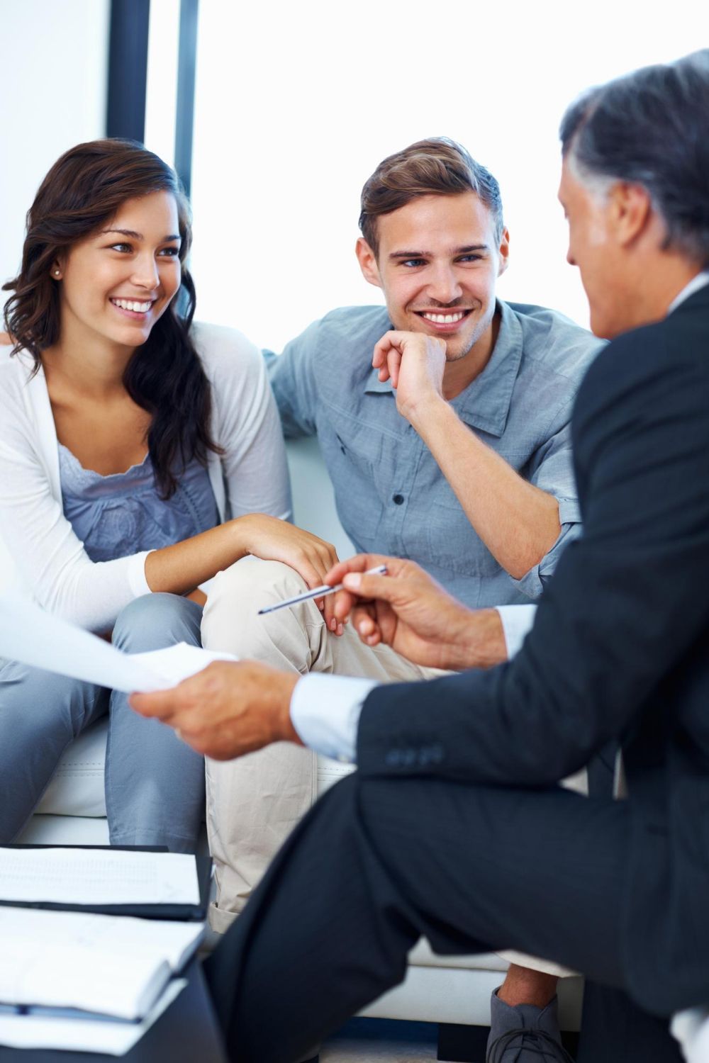 Couple smiling while reviewing documents with a professional in an office setting.