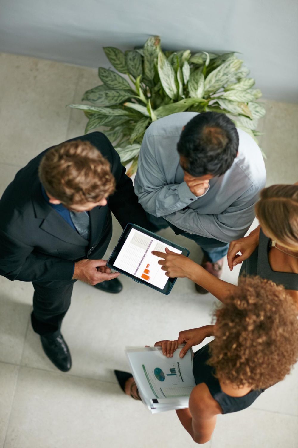 Three people reviewing data on a tablet and paper, gathered around a plant.