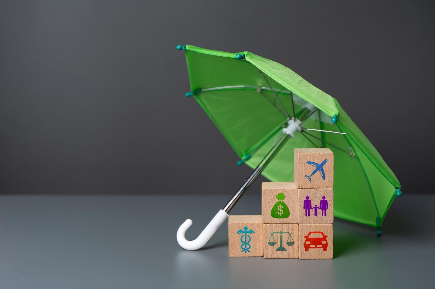 Green umbrella over stacked blocks with icons for insurance protection.