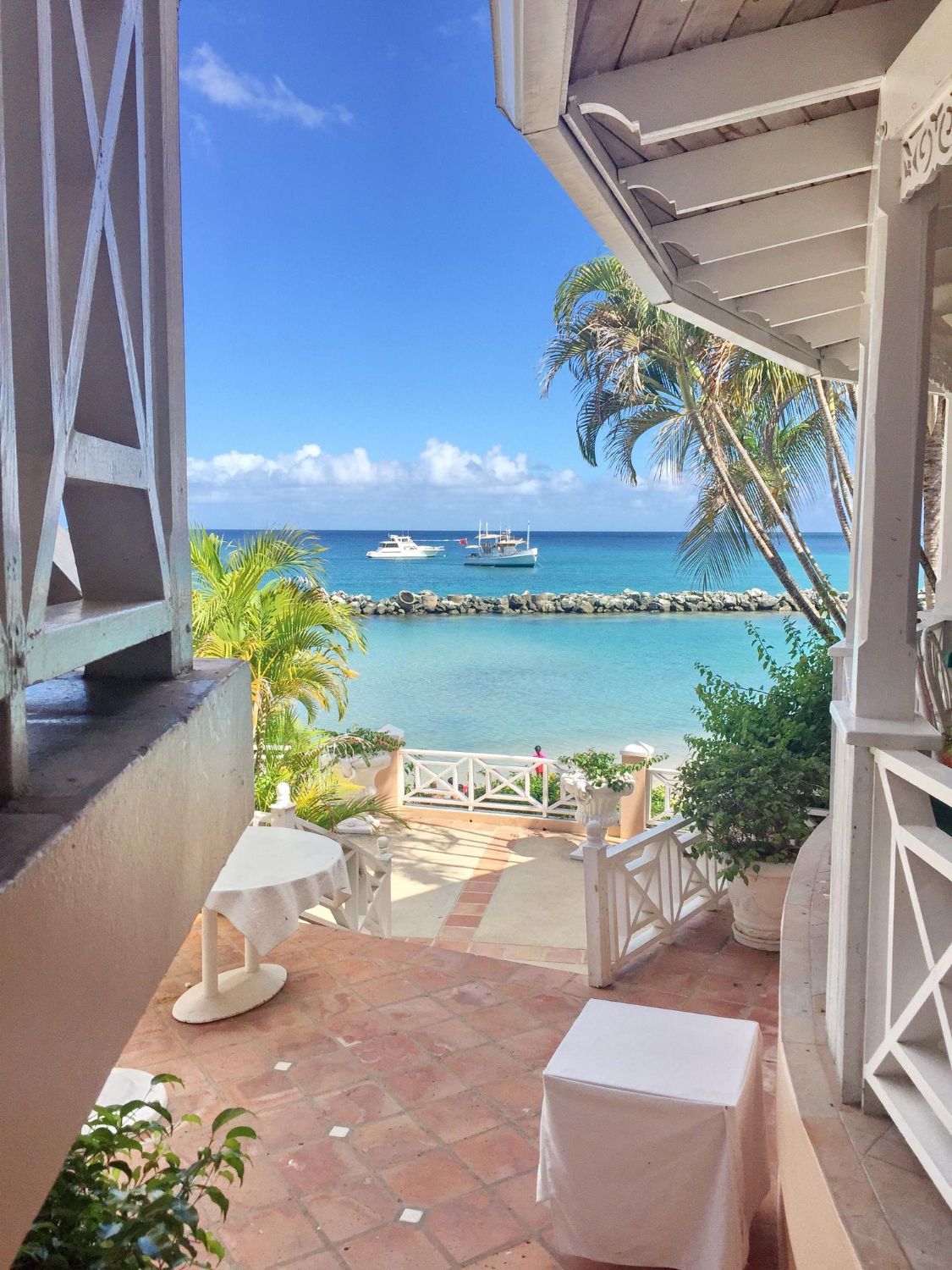 Patio overlooking a tropical beach with turquoise water and boats under a bright blue sky.