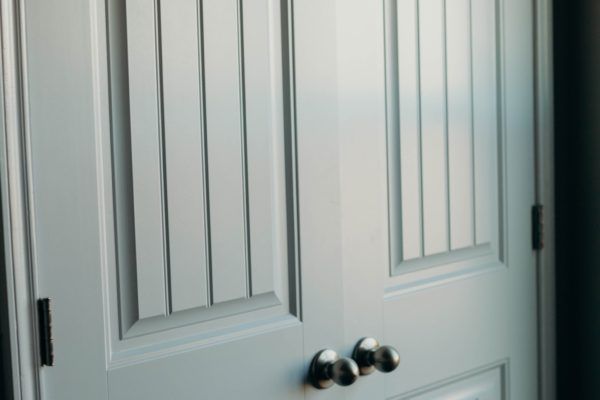 White paneled door with vertical grooves, dark hardware, and silver doorknobs.