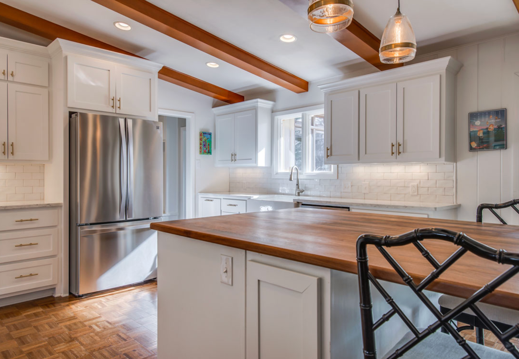 Bright white kitchen with stainless steel appliances, wood island, and wooden ceiling beams.