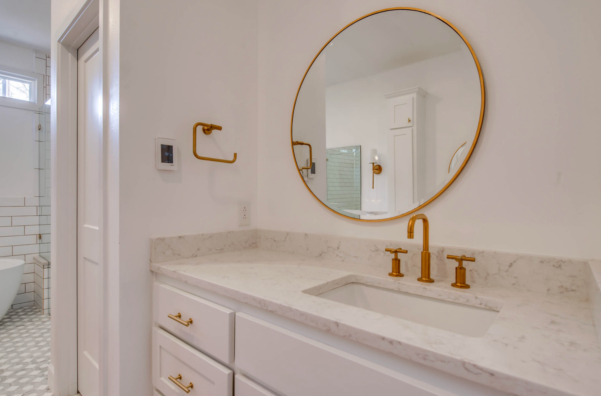 Bathroom with white cabinets, marble countertop, gold fixtures, and round mirror.