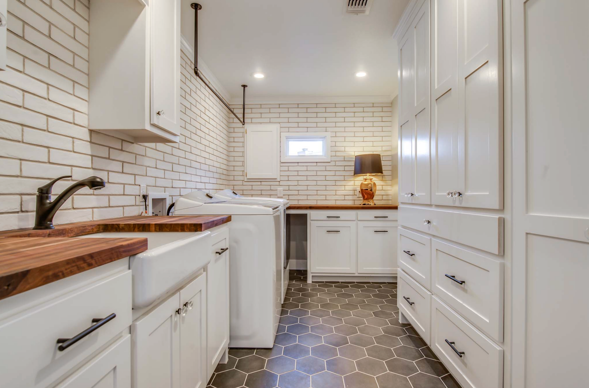 Laundry room with white cabinets, brick tile, dark countertops, and patterned floor.