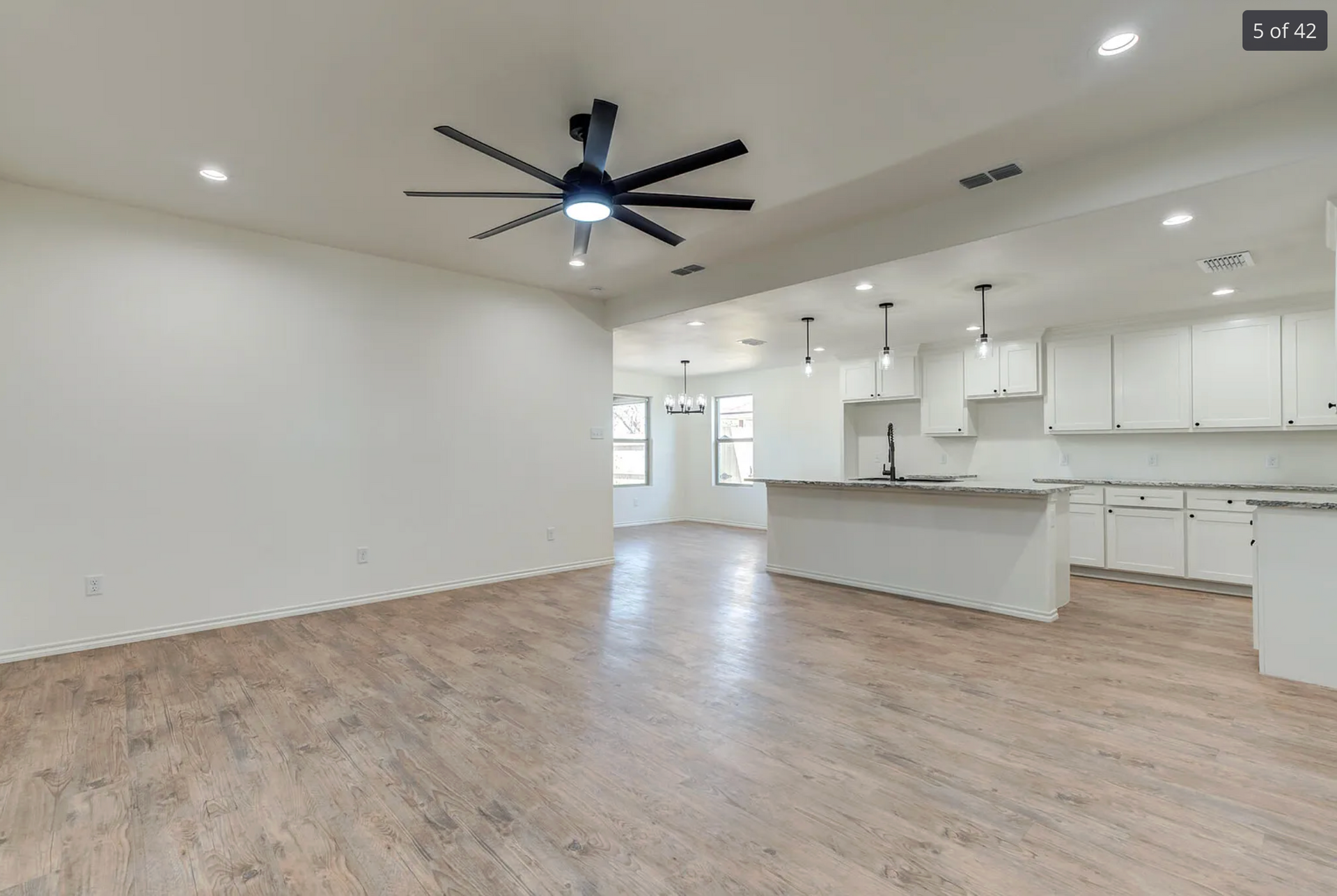 Spacious, modern kitchen and living area with hardwood floors and a black ceiling fan.