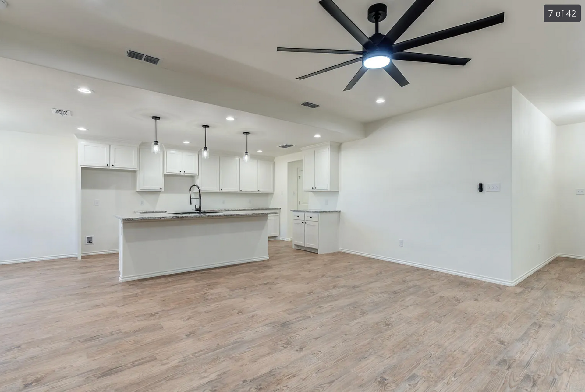 Open-concept kitchen with white cabinets, island, and wood-look flooring. A black ceiling fan is visible.