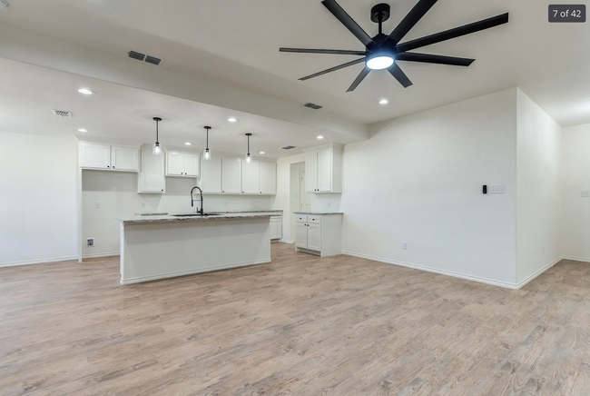 Open-concept kitchen with white cabinets, island, and wood-look flooring. A black ceiling fan is visible.
