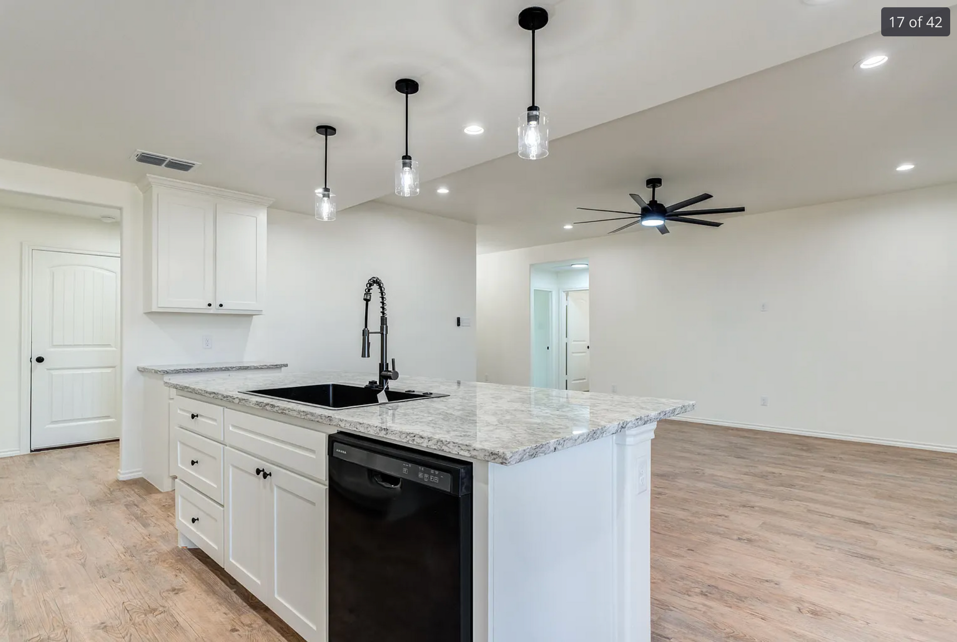 White kitchen island with a black sink and dishwasher, pendant lights, and wood flooring.