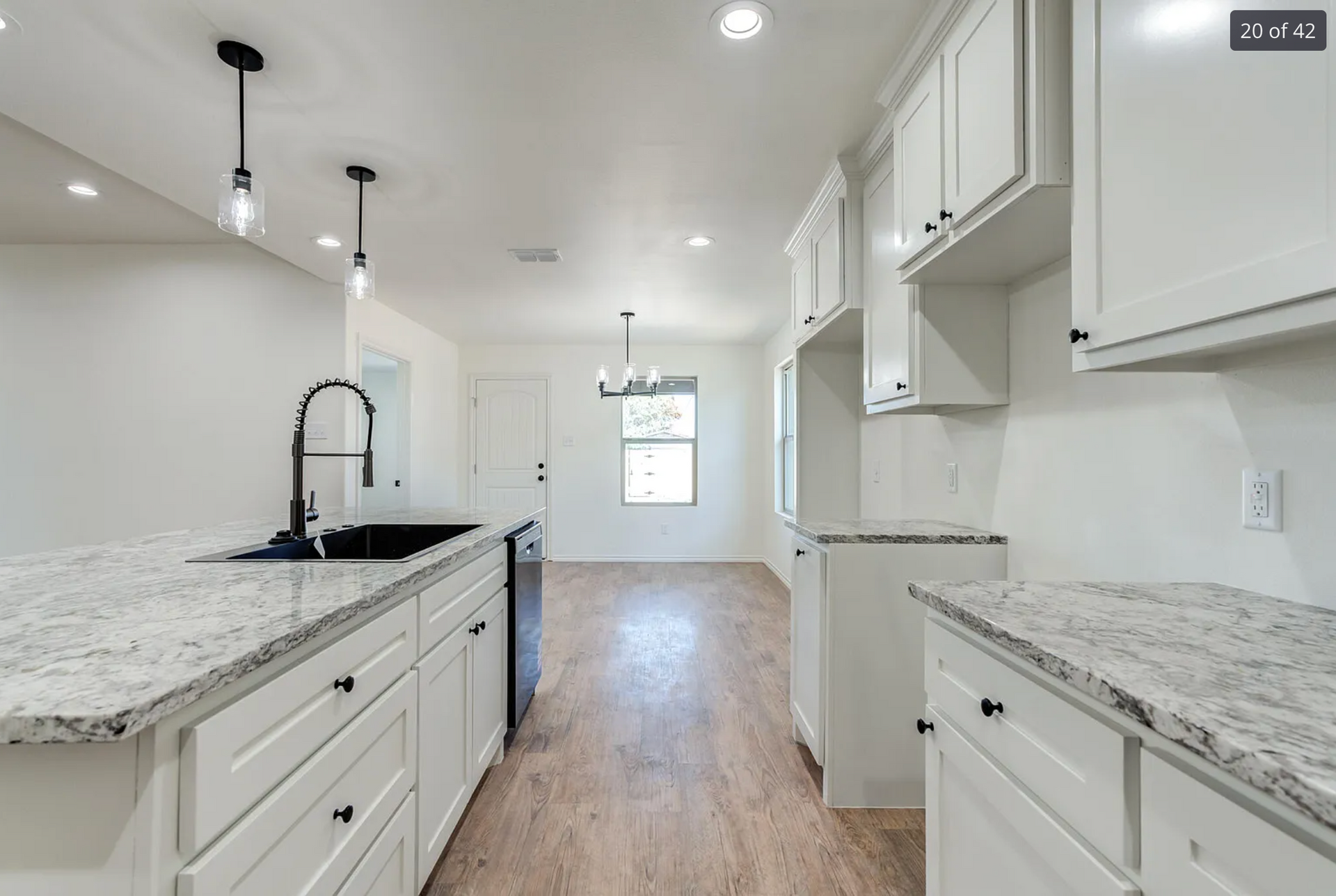 Bright white kitchen with granite countertops, black faucet, and pendant lights.