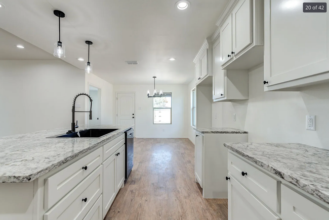 Bright white kitchen with granite countertops, black faucet, and pendant lights.