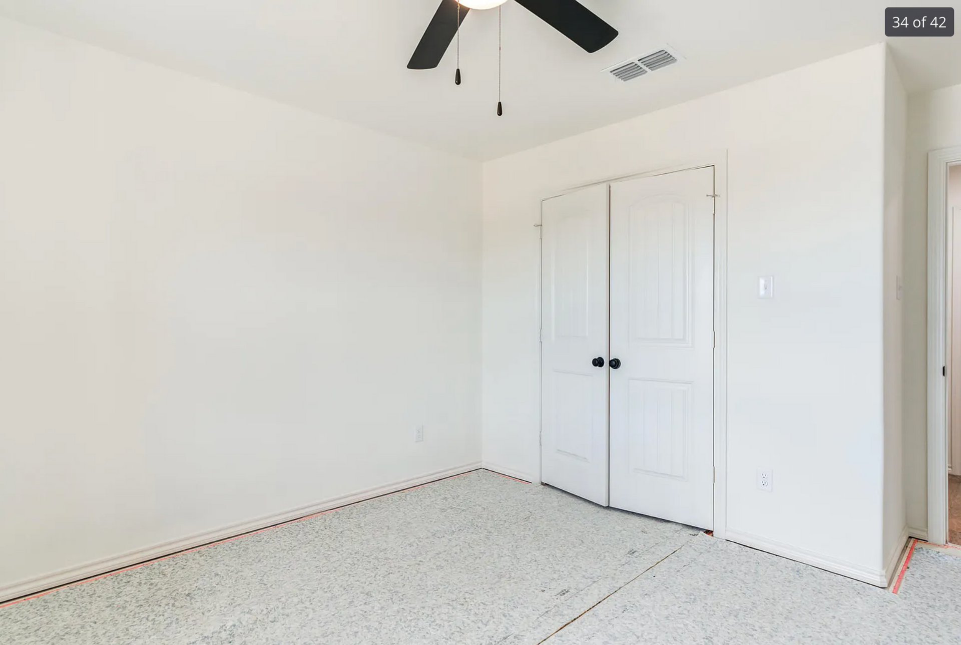 Empty bedroom with white walls, carpet, and closet doors. A ceiling fan is visible.