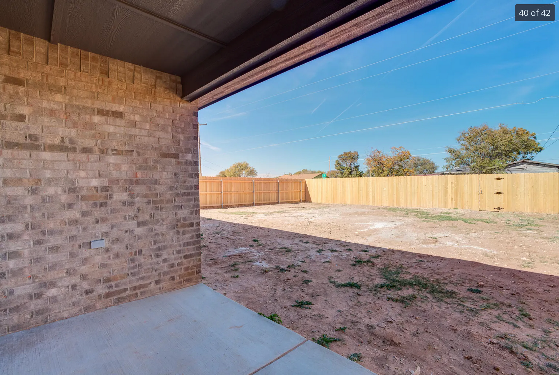 Brick patio and backyard, wooden fence, clear sky.