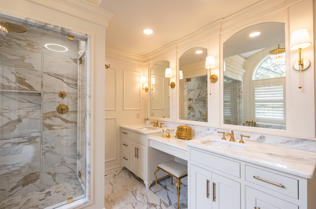 Luxurious white bathroom with marble shower, gold fixtures, and arched mirrors.