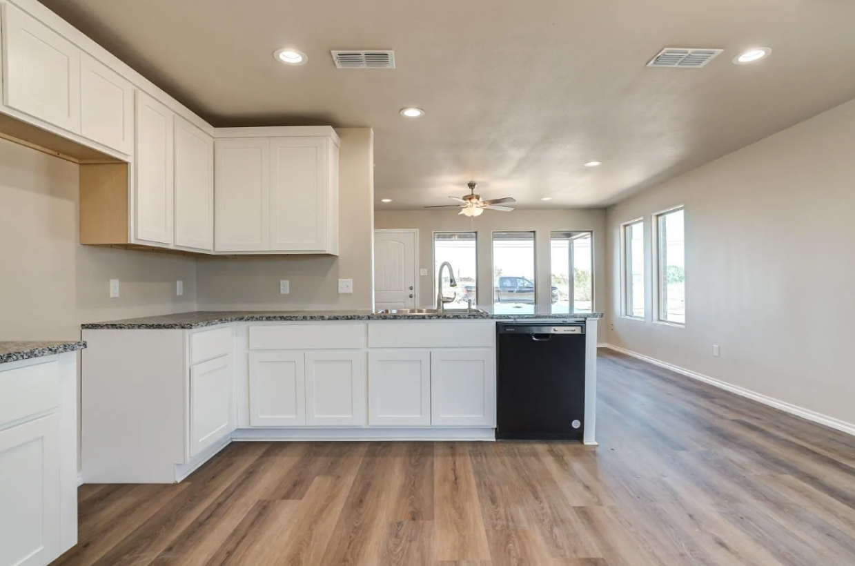 Modern kitchen with white cabinets, dark speckled countertops, black dishwasher, and light wood flooring.