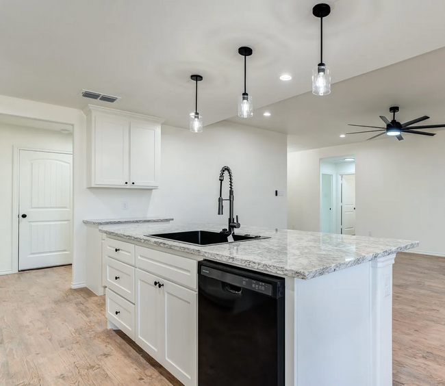 White kitchen island with granite countertop, black sink and appliances, and pendant lights.