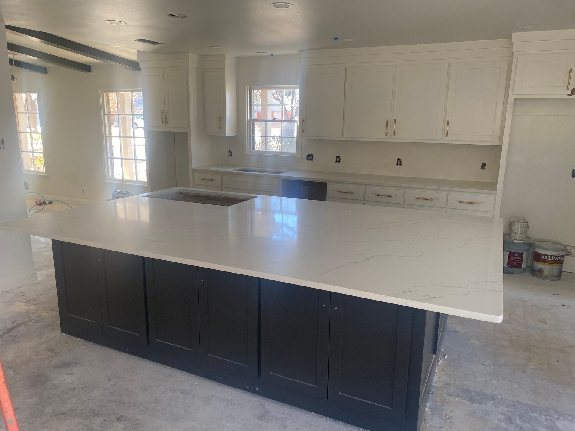 Kitchen under construction with a black island, white countertops, and white cabinets.